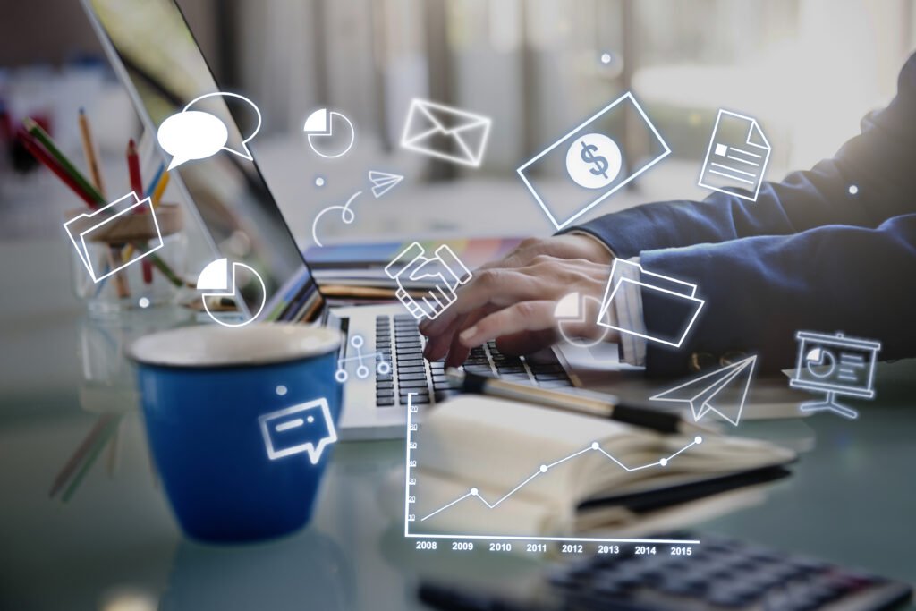 A business man writing on a laptop with icons around him colored blue and white