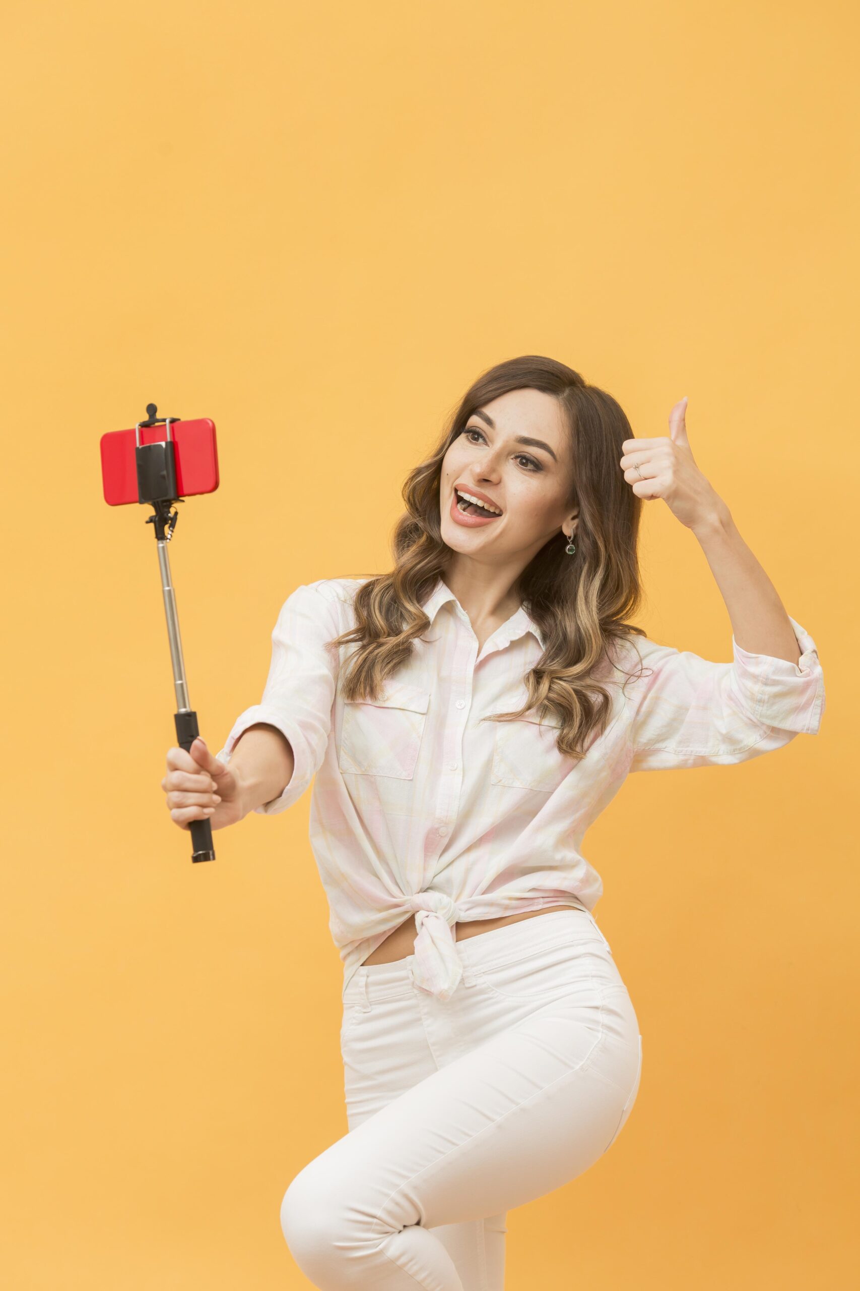 A woman filming her self using her phone on self stick and making a thumbs up