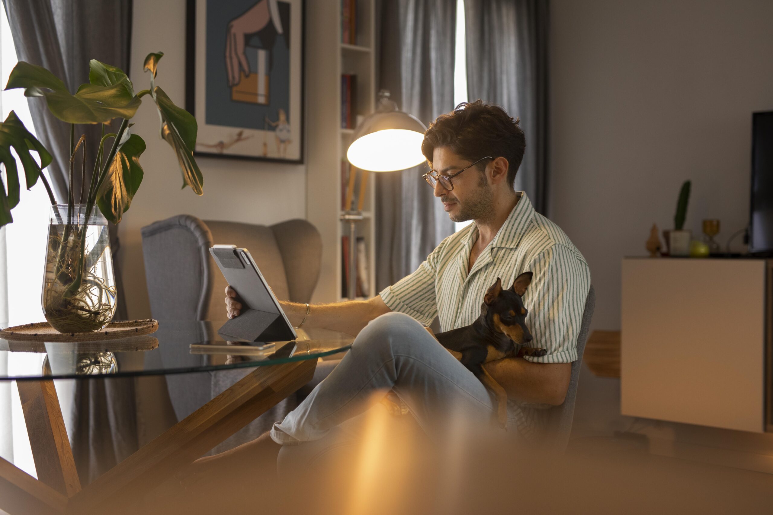 A man his dog setting on his chair with his dog on his legs and working on his laptop