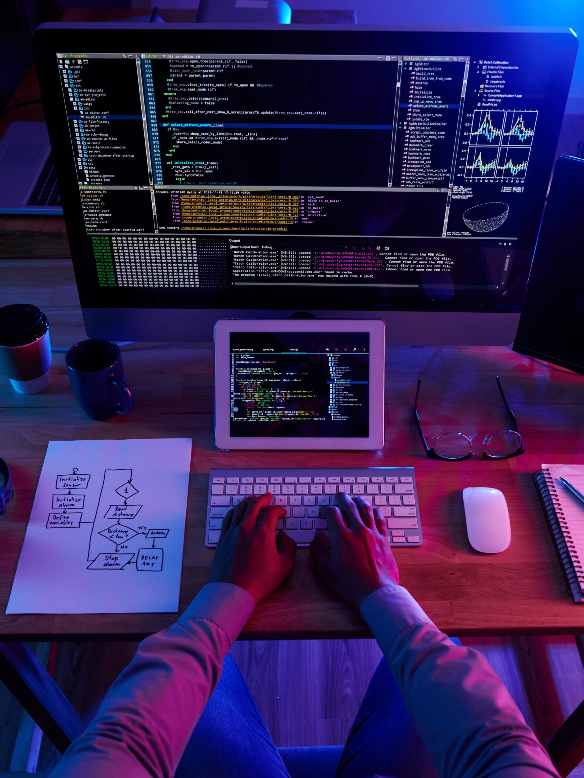 a wide angle of a man hands writing codes on his PC and his Ipad in front of him