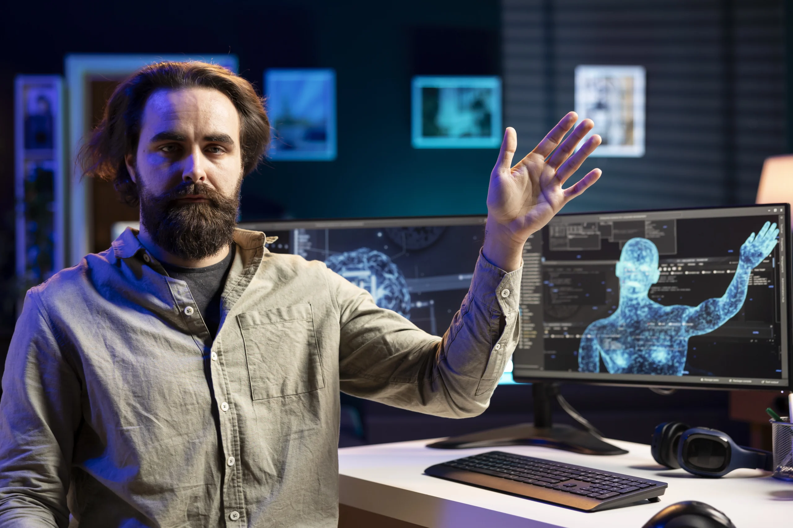 Tech engineer raising his left hand, with a computer screen in the background displaying a holographic human figure surrounded by digital tech elements.