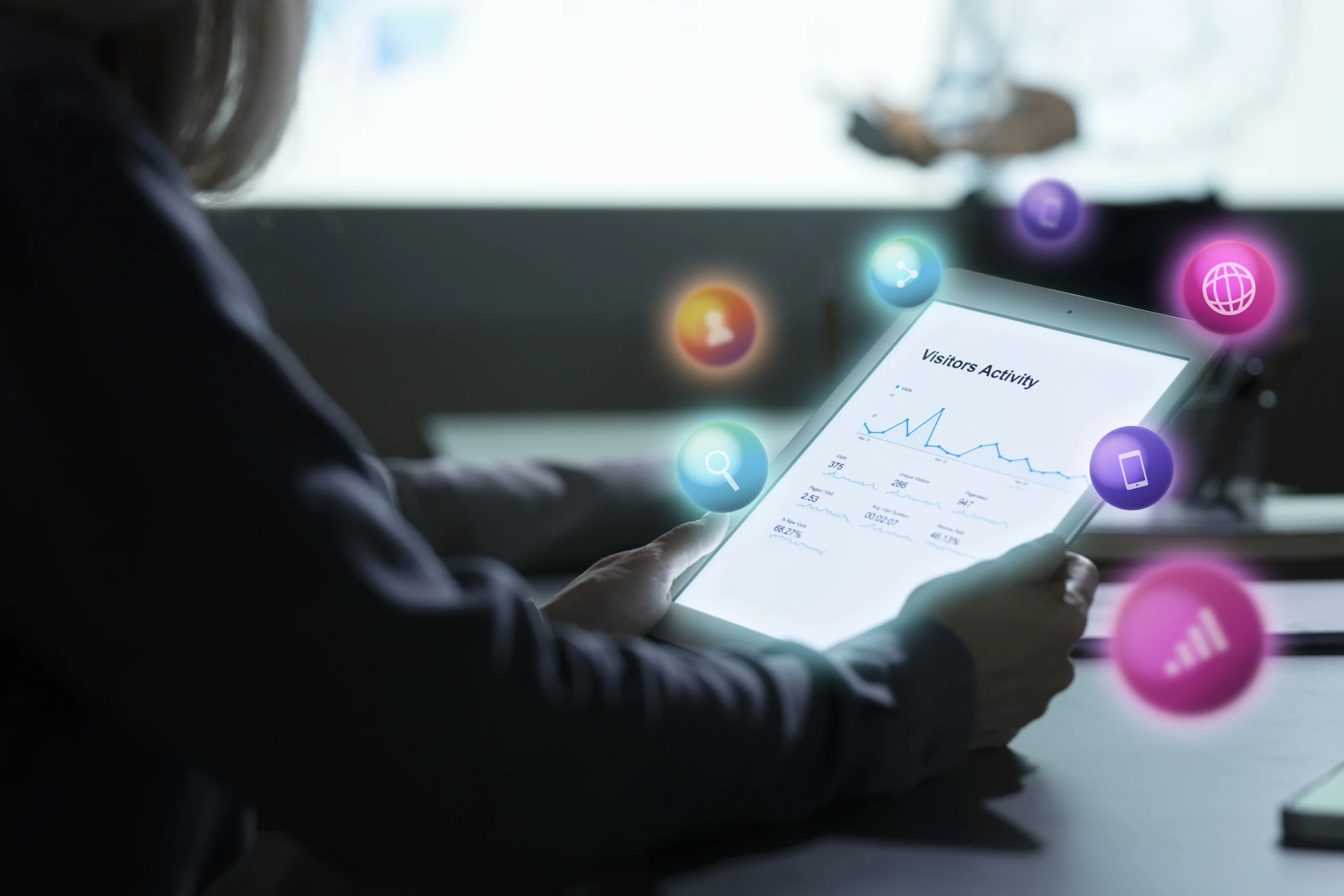 A woman in a meeting holds a tablet displaying data insights, with the text u0022Visitors Activityu0022 and various social media icons surrounding the screen. The scene highlights digital advertising trends, with the tablet showcasing key insights on social media engagement and visitor activity.