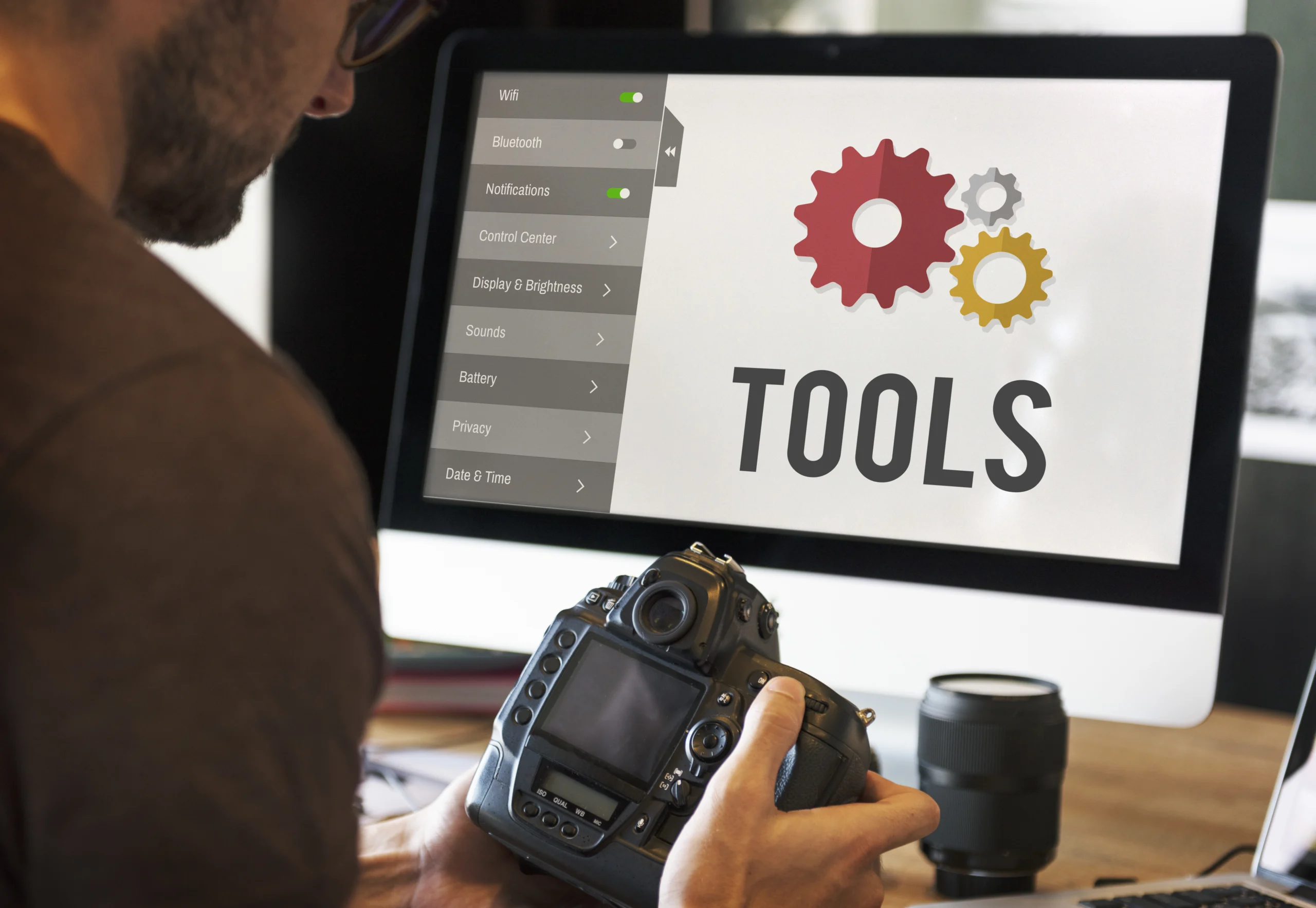 Photographer seated at his desk, holding a camera with a focused expression. His computer screen displays various tools and settings icons, highlighting his creative workspace. The scene captures the blend of artistry and technology in photography.






