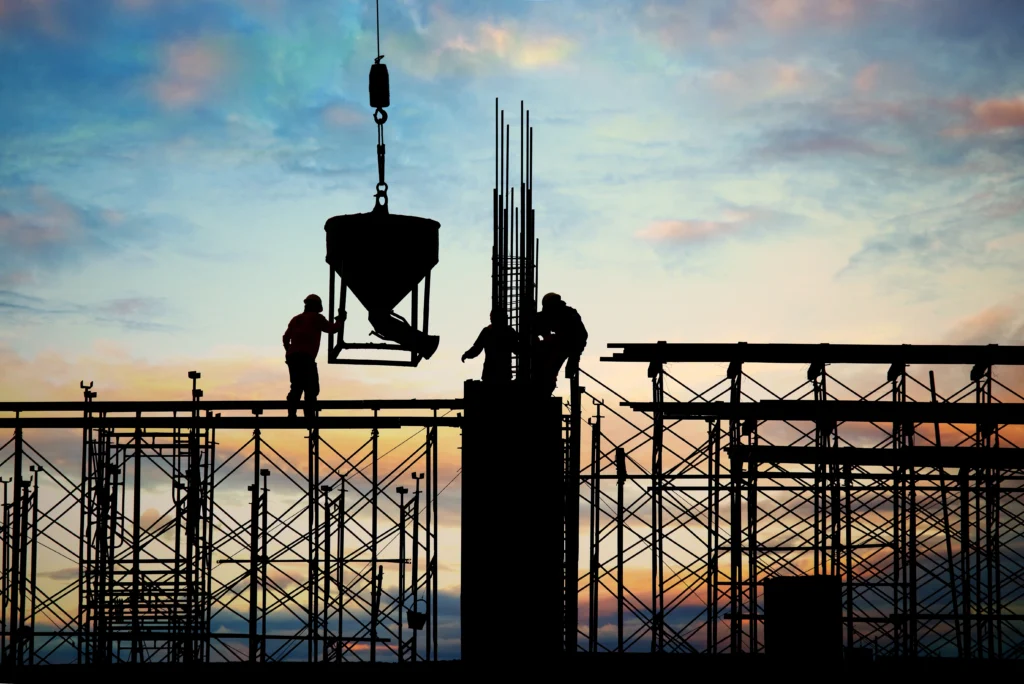 A construction site at sunset, with a worker holding a drill against a backdrop of warm, glowing light.