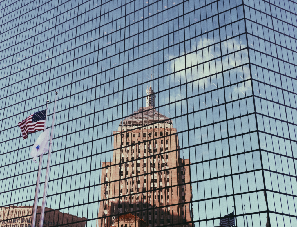 A stunning glass building in Texas reflects the image of another iconic structure, creating a captivating visual interplay. The vibrant American flag proudly stands beside it, adding a touch of patriotism to the scene. This architectural marvel not only showcases modern design but also serves as a striking reminder of the country's spirit and resilience.