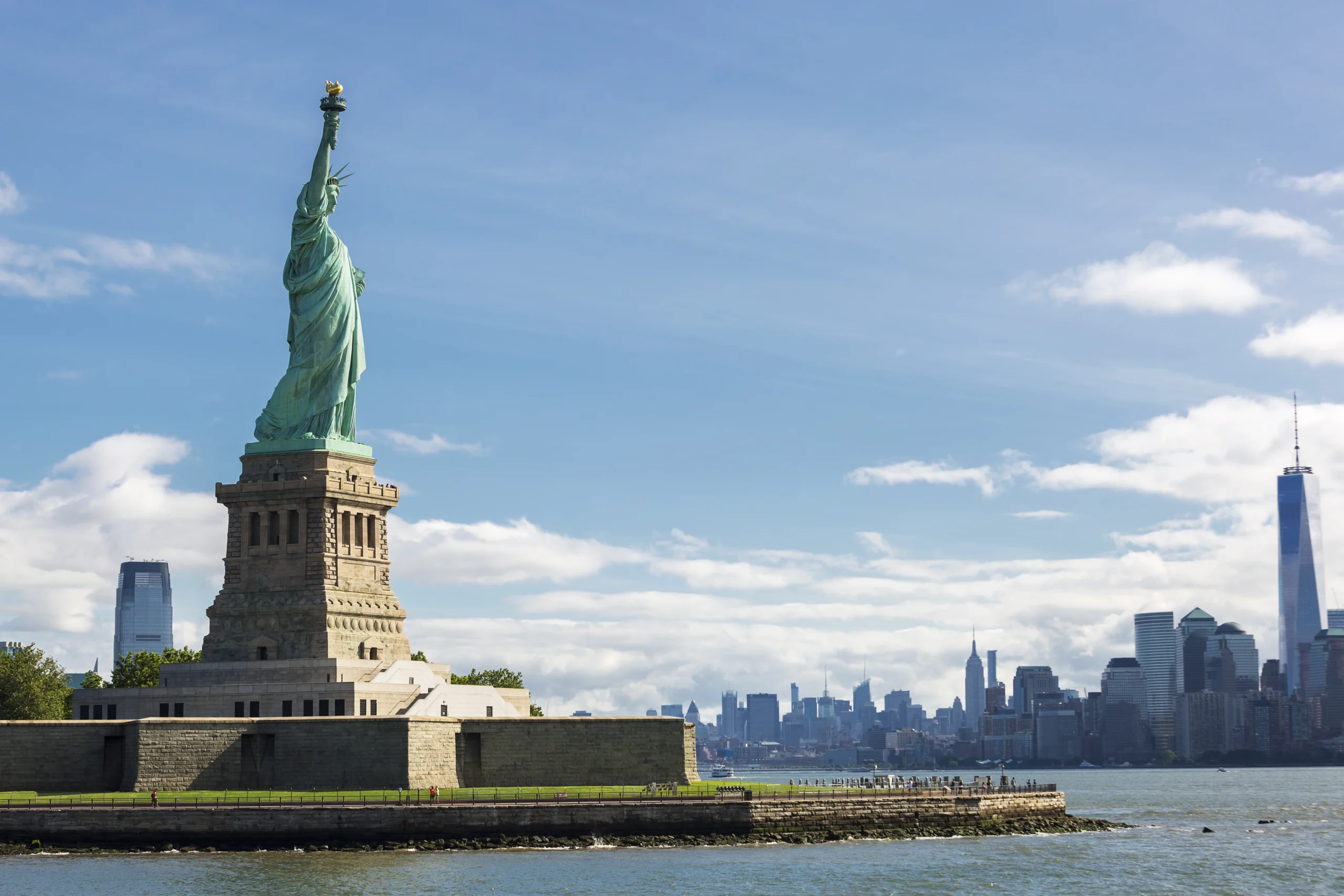 A wide-angle view of the Statue of Liberty with the New York City skyline in the background, capturing both iconic landmarks in a sweeping, scenic shot.nnnnnn